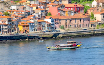 Boat cruising on Douro River with colorful Porto buildings in the background.