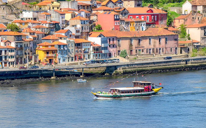 Boat cruising on Douro River with colorful Porto buildings in the background.