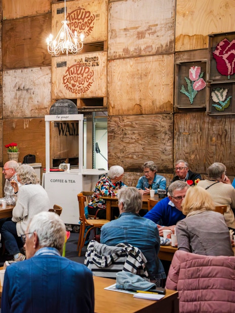 Group enjoying coffee at Tulip Experience Amsterdam with mural backdrop.