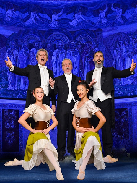 Opera singers and dancers performing in front of a blue-lit mural at night.