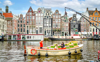 Guests enjoying tulip cruise on Amsterdam canal with historic buildings in background.