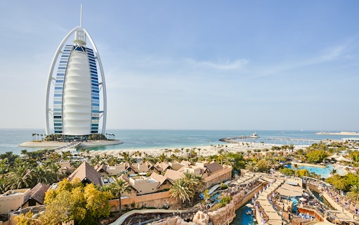 Family enjoying water slide at Wild Wadi Water Park, Dubai, with Burj Al Arab in background.