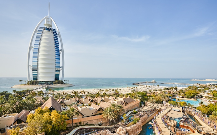 Family enjoying water slide at Wild Wadi Water Park, Dubai, with Burj Al Arab in background.