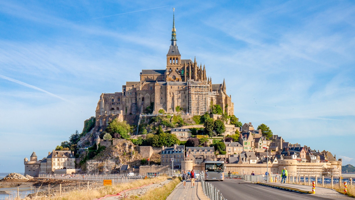 Mont Saint Michel abbey with tourists walking on the causeway, France.