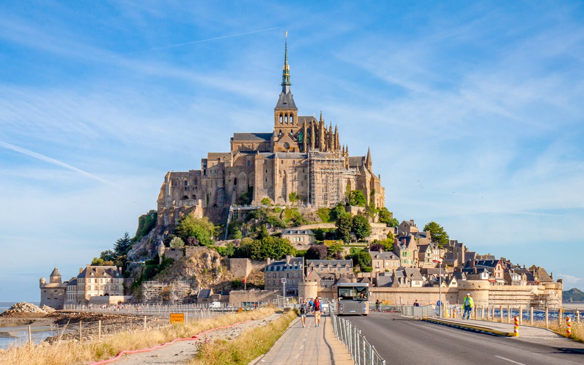 Mont Saint Michel abbey with tourists walking on the causeway, France.