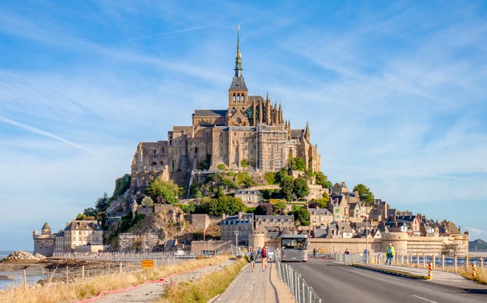 Mont Saint Michel abbey with tourists walking on the causeway, France.