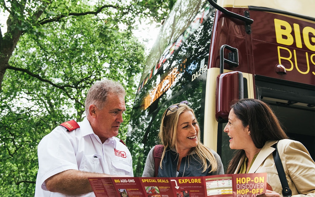 Tourists with a guide in front of a Los Angeles hop-on hop-off bus, holding a map.