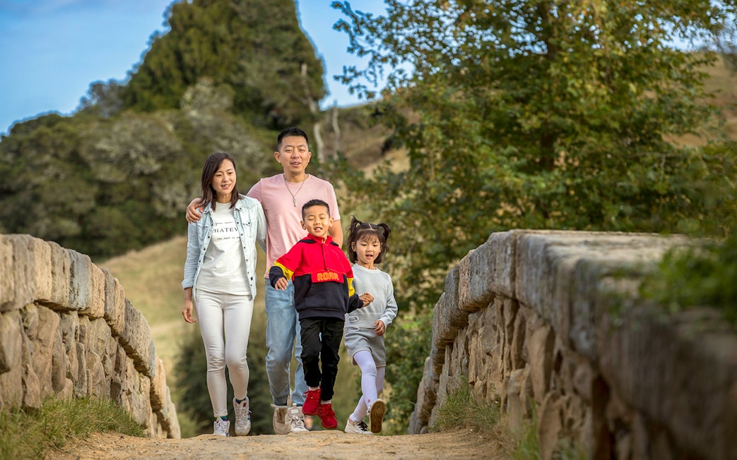 Family walking on a stone bridge at Hobbiton Movie Set, New Zealand.