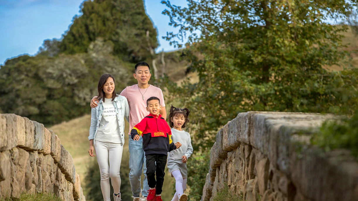 Family walking on a stone bridge at Hobbiton Movie Set, New Zealand.