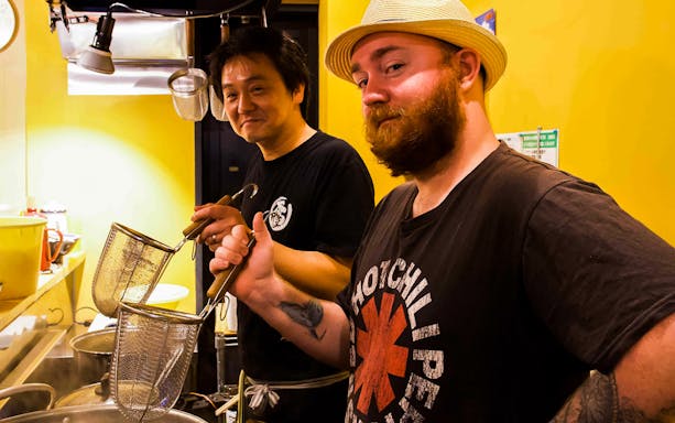 Two chefs holding noodle strainers in a ramen kitchen during a cooking experience.