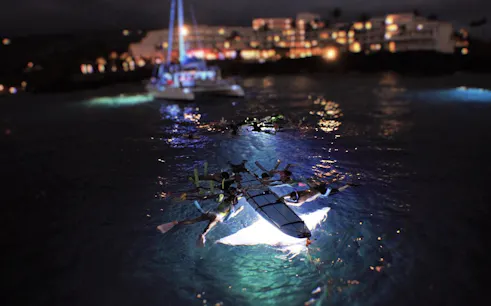 Snorkelers observe manta rays illuminated by lights during a night tour in the ocean.