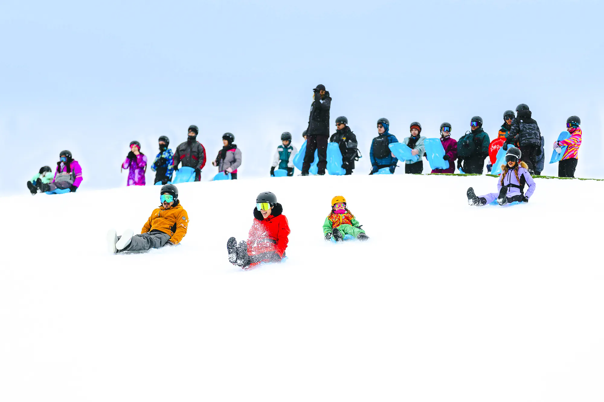 People sledding on snow at Farellones Park, Santiago, with others waiting in line.