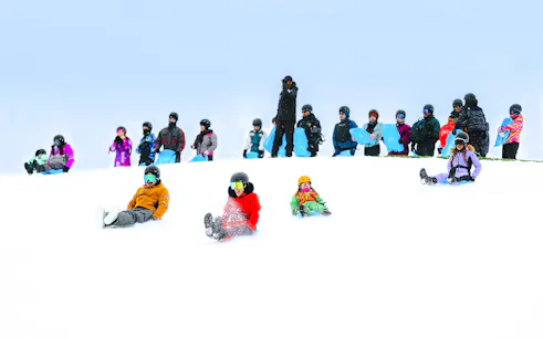 People sledding on snow at Farellones Park, Santiago, with others waiting in line.