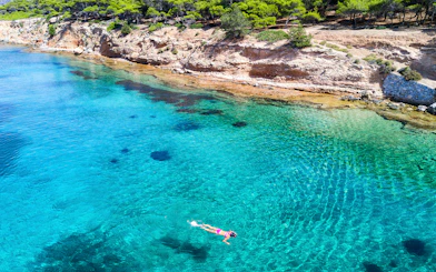 Snorkeler exploring clear waters near rocky coast of Aegina Island, Greece.