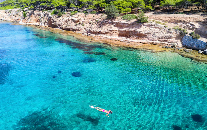 Snorkeler exploring clear waters near rocky coast of Aegina Island, Greece.