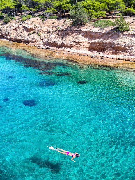 Snorkeler exploring clear waters near rocky coast of Aegina Island, Greece.