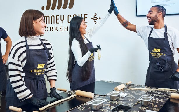 Participants enjoying a Chimney Cake workshop in Budapest, preparing dough with rolling pins.