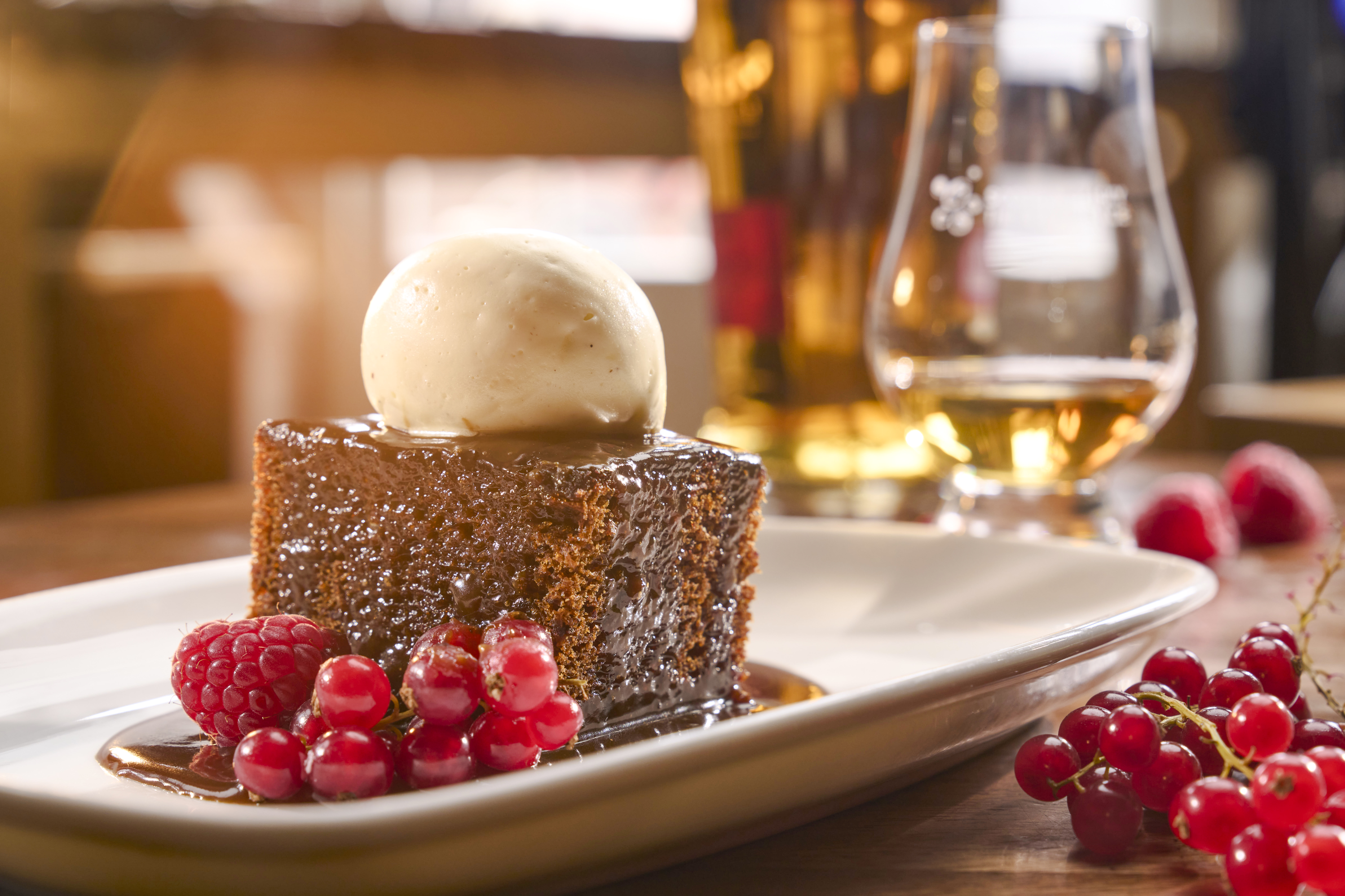 Sticky toffee pudding with ice cream and berries, paired with a glass of Scotch whisky.