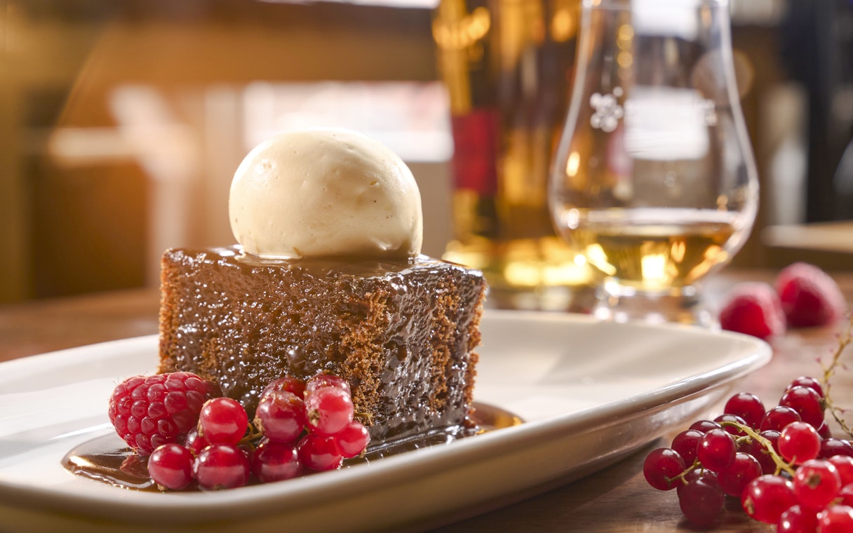 Sticky toffee pudding with ice cream and berries, paired with a glass of Scotch whisky.