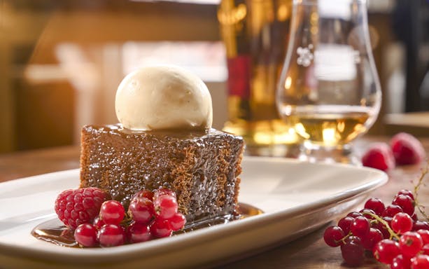 Sticky toffee pudding with ice cream and berries, paired with a glass of Scotch whisky.