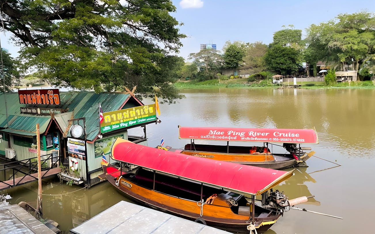 Mae Ping River Cruise boats docked by a riverside cafe in Chiang Mai.