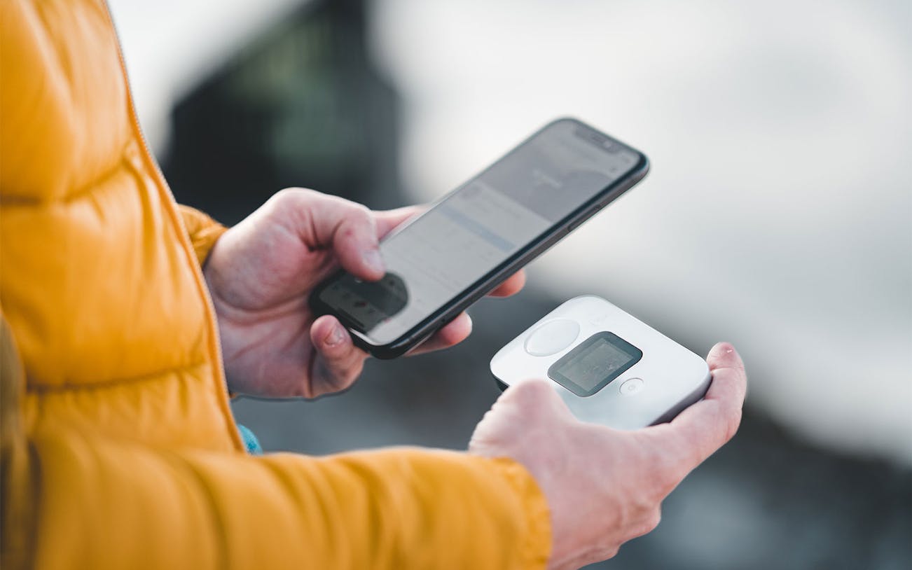 Hands holding a smartphone and a portable 4G Wi-Fi router.