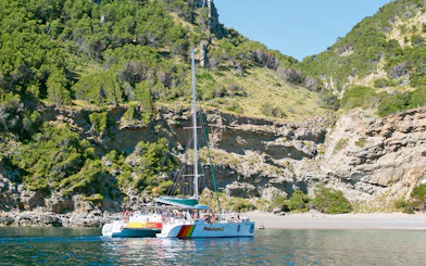 Catamaran sailing near rocky coastline in Alcudia, Mallorca.