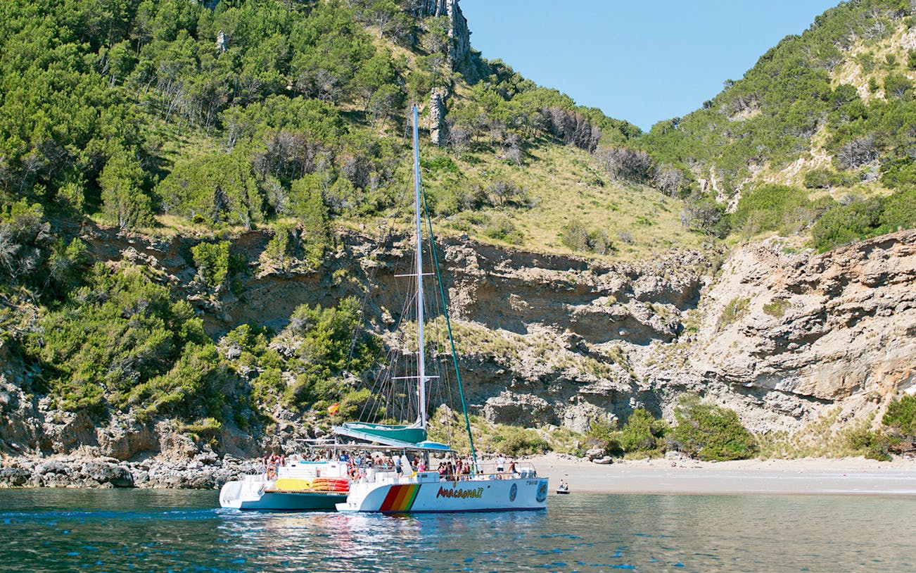 Catamaran sailing near rocky coastline in Alcudia, Mallorca.