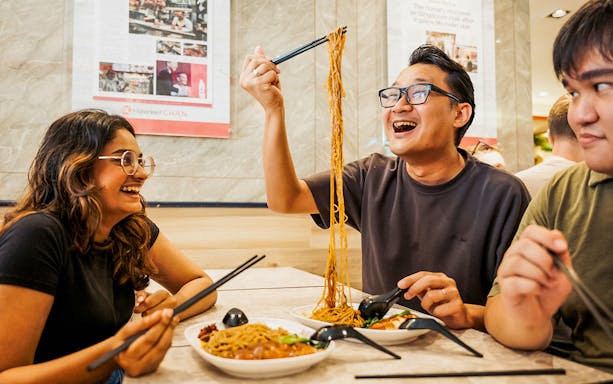 People enjoying noodles at a Michelin-rated hawker center during a guided food tour.