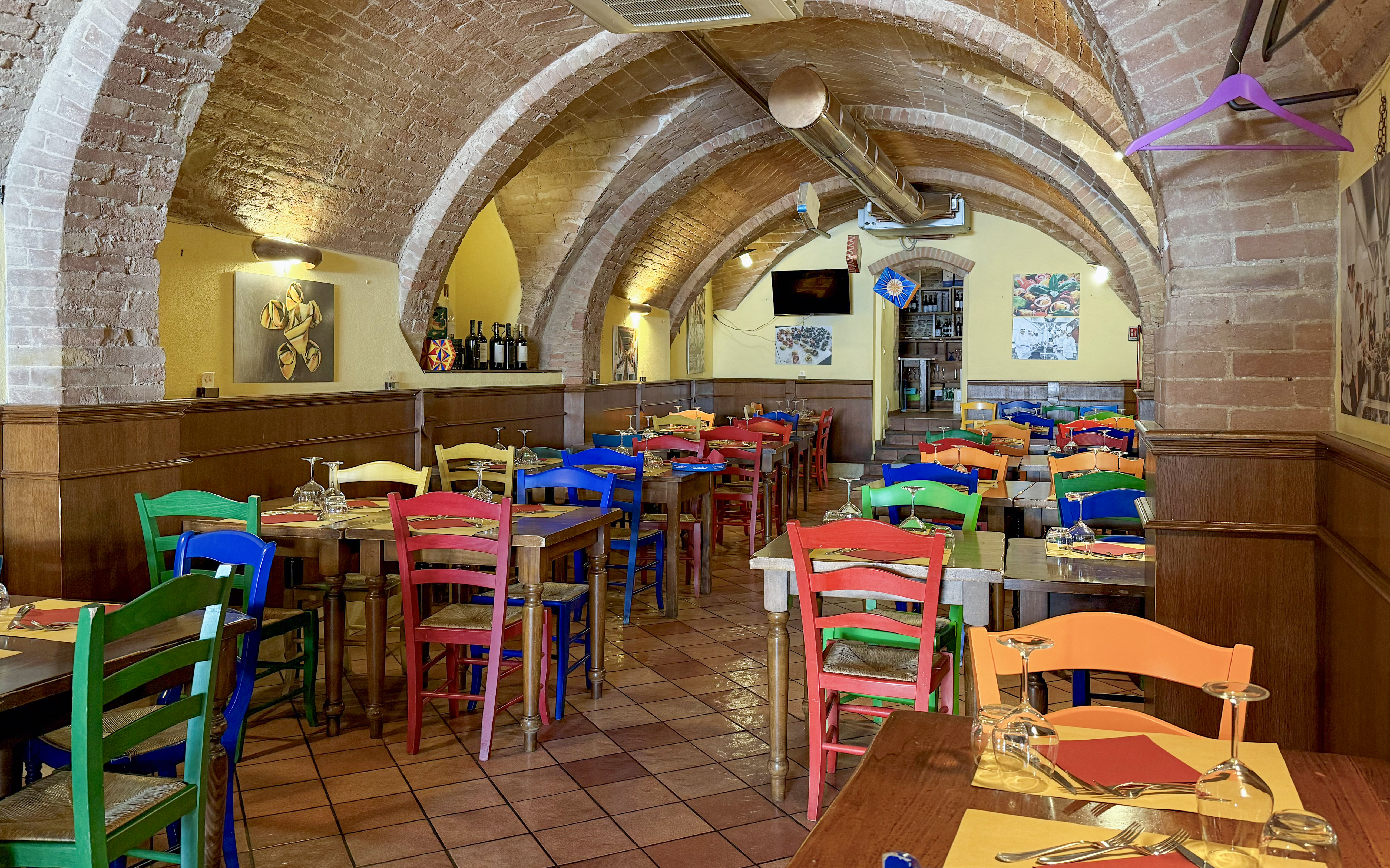 Colorful chairs and tables inside a brick-arched cafe in Siena for pasta cooking classes.