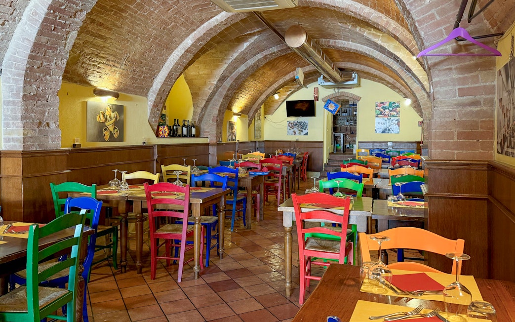 Colorful chairs and tables inside a brick-arched cafe in Siena for pasta cooking classes.