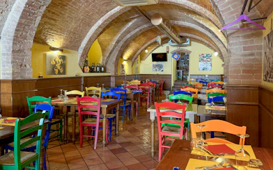 Colorful chairs and tables inside a brick-arched cafe in Siena for pasta cooking classes.