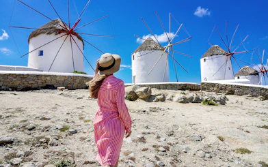 Woman in a hat walking towards iconic windmills on Mykonos, Greece.