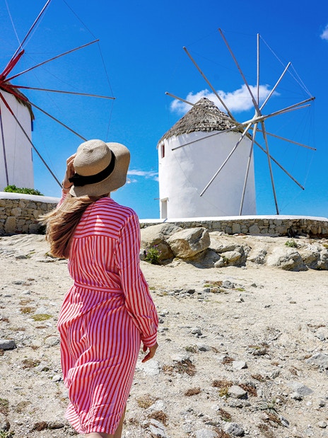 Woman in a hat walking towards iconic windmills on Mykonos, Greece.