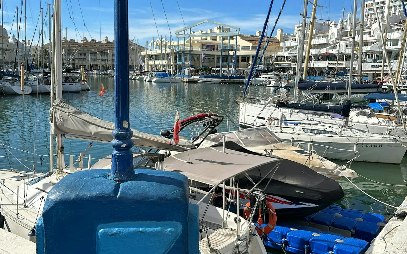 Benalmádena marina with sailboats and waterfront buildings, part of the Don Quixote city exploration game.