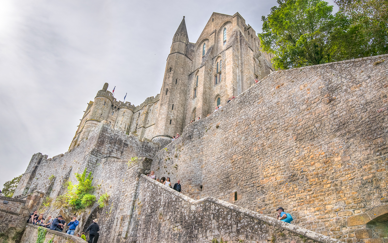 Mont Saint-Michel Abbey stone walls with visitors on steps, Normandy, France.