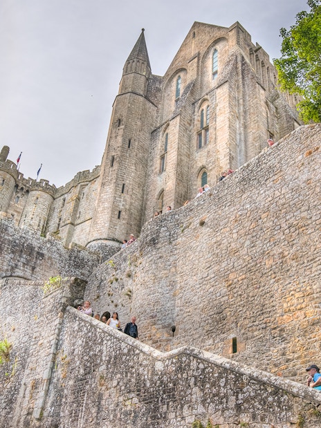 Mont Saint-Michel Abbey stone walls with visitors on steps, Normandy, France.