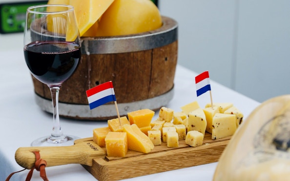 Wine glass and Dutch cheese with flags on a wooden board, Amsterdam canal cruise.