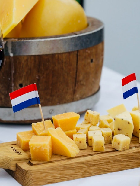 Wine glass and Dutch cheese with flags on a wooden board, Amsterdam canal cruise.