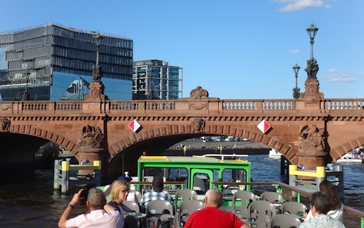 Sightseeing cruise boat passing under a historic bridge in East Berlin.
