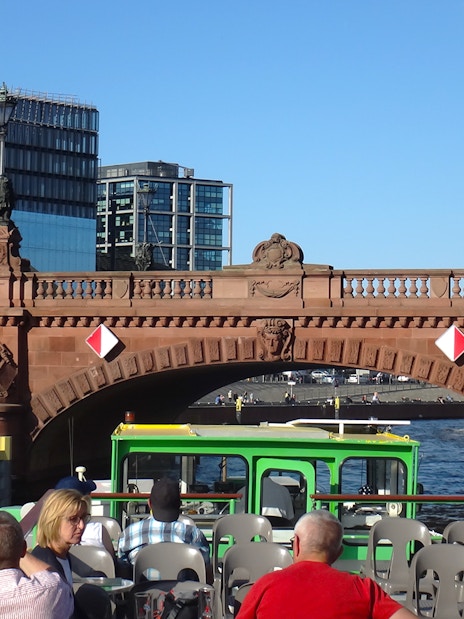 Sightseeing cruise boat passing under a historic bridge in East Berlin.