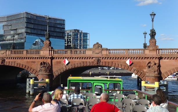 Sightseeing cruise boat passing under a historic bridge in East Berlin.