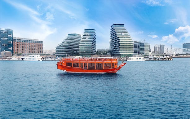 Dhow boat cruising in Abu Dhabi with modern buildings in the background.