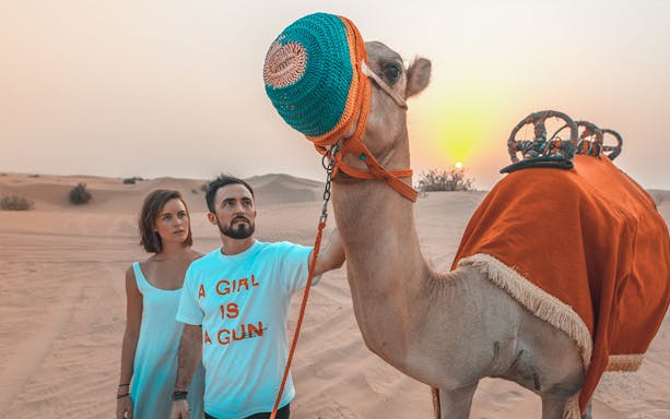 Camel ride at desert safari with two people at sunset.