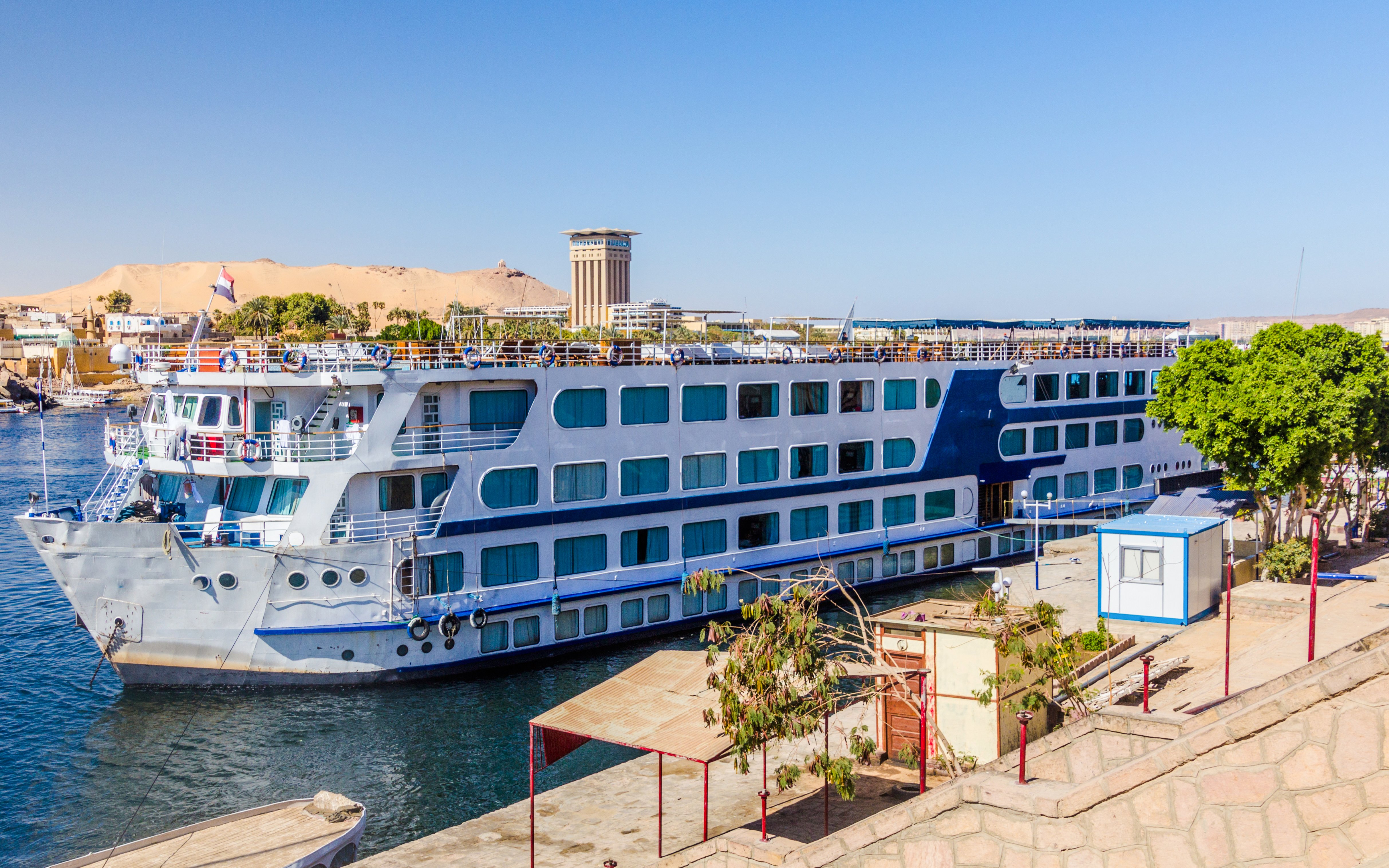Cruise ship docked on the Nile River in Aswan, Egypt with desert backdrop.
