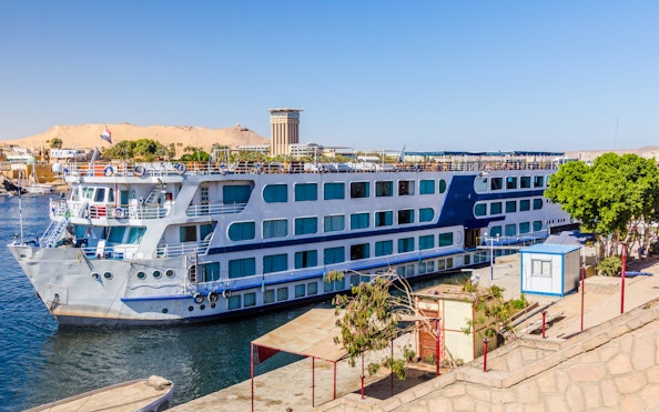 Cruise ship docked on the Nile River in Aswan, Egypt with desert backdrop.
