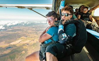 Tandem skydivers preparing to jump over Airlie Beach with scenic landscape below.