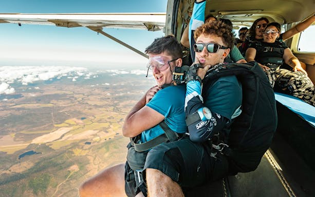 Tandem skydivers preparing to jump over Airlie Beach with scenic landscape below.