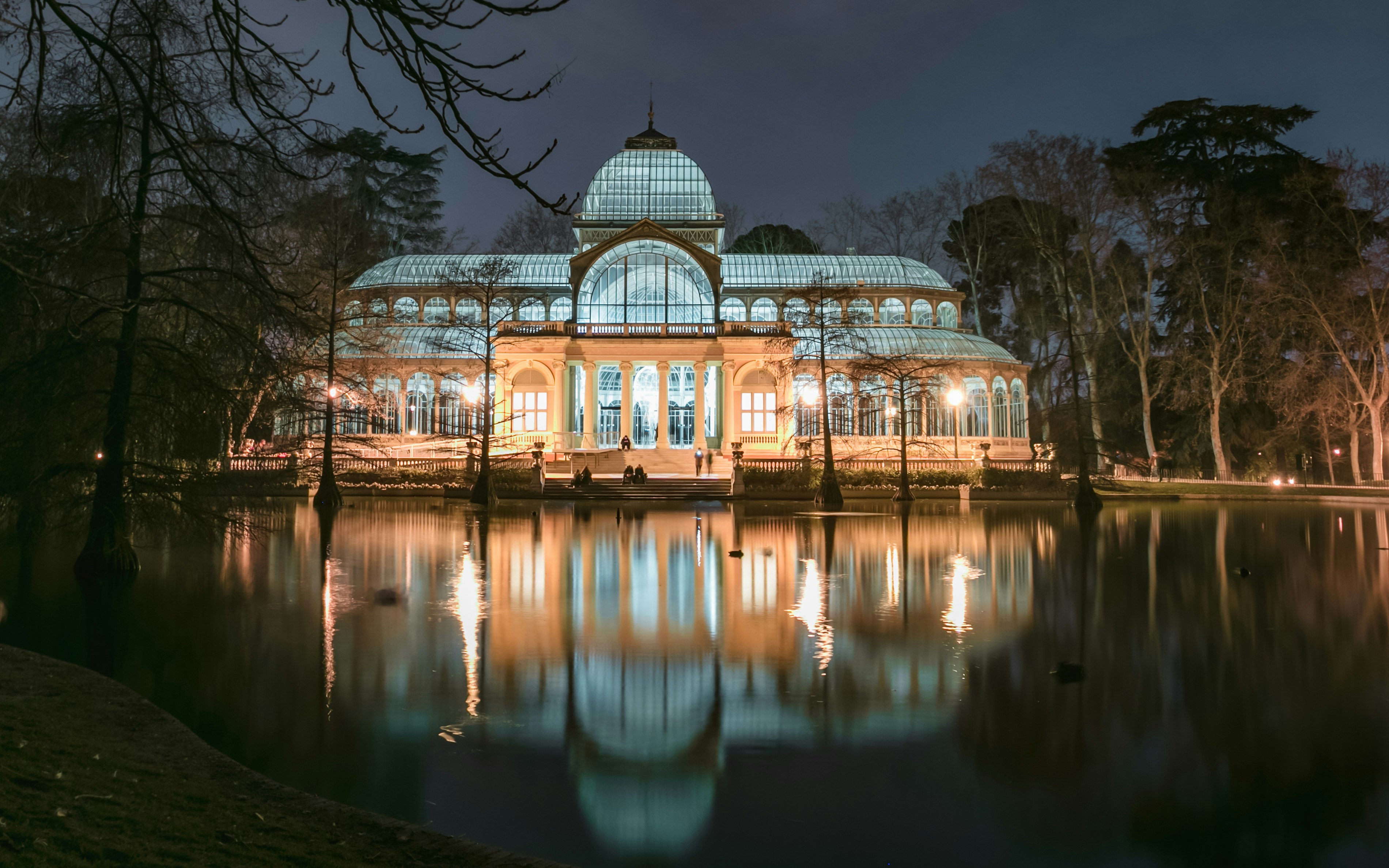 Crystal Palace illuminated at night, reflecting in the lake at Retiro Park, Madrid, Spain.