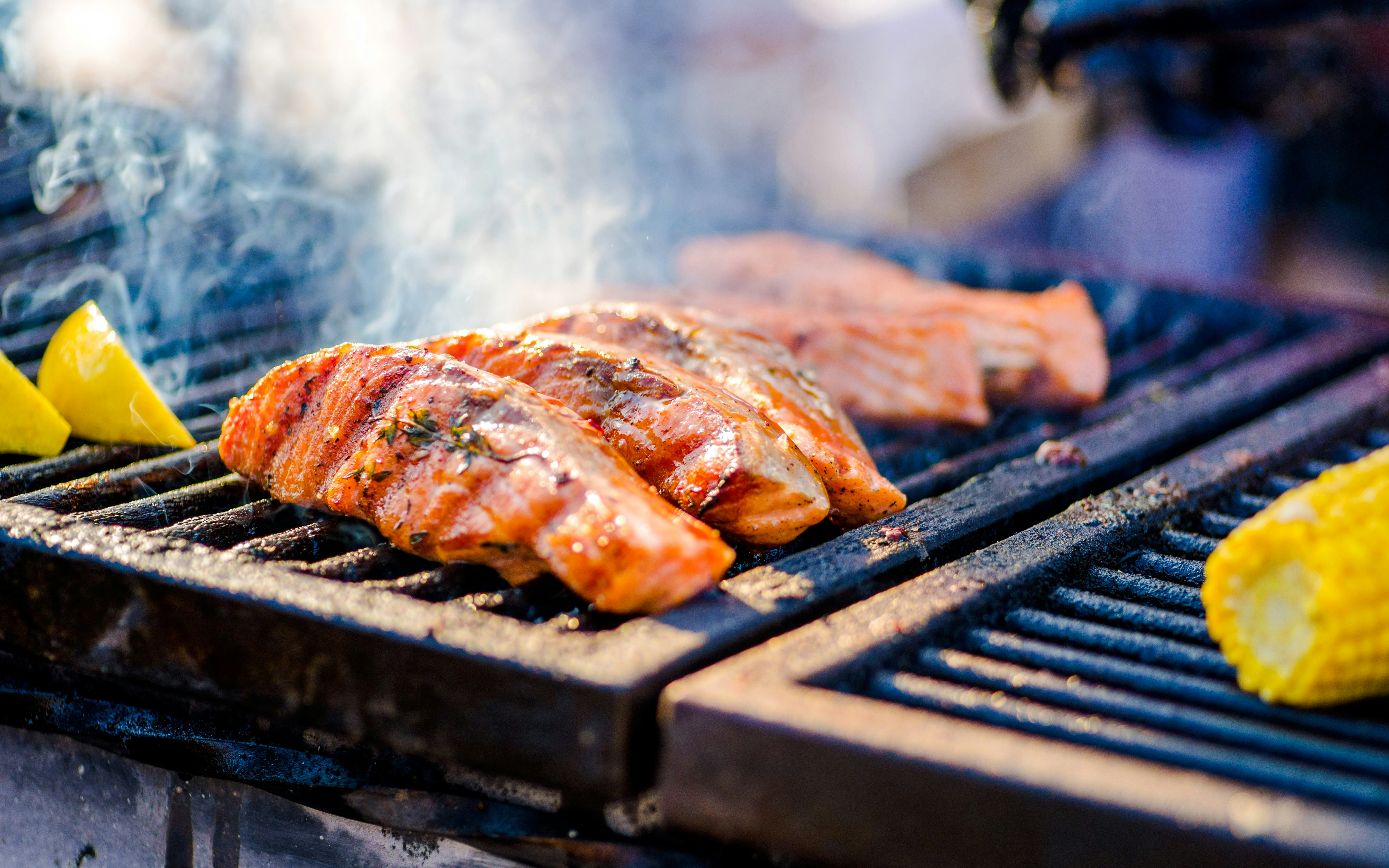 Grilled fish on an open fire barbecue with lemon wedges and corn.